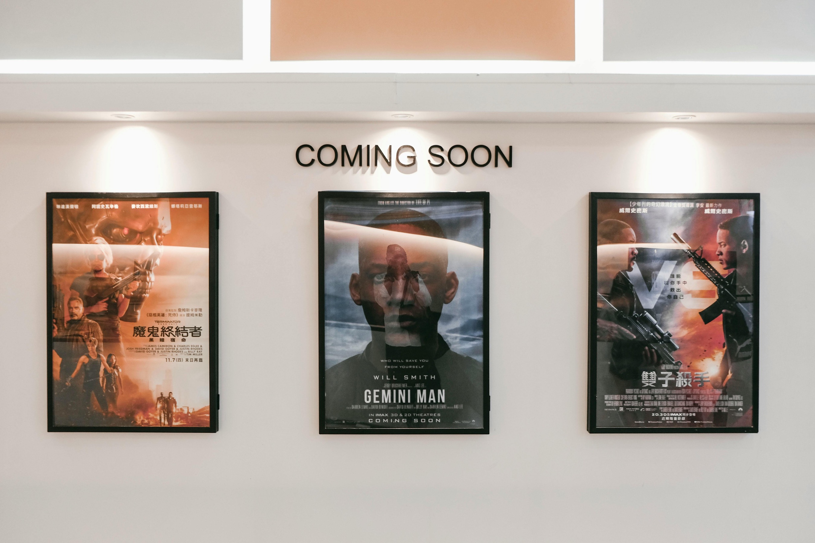 Three movie posters displayed on a wall, featuring titles in Chinese and English. The center poster is for 'Gemini Man' starring Will Smith, with the phrase 'Coming Soon' above the posters.